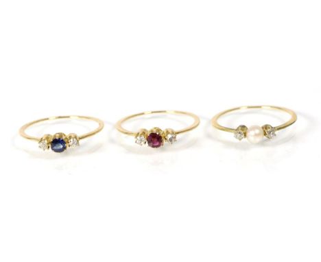 A set of three rings, comprising; a ruby and diamond three stone ring, a pearl and diamond three stone ring and a sapphire an