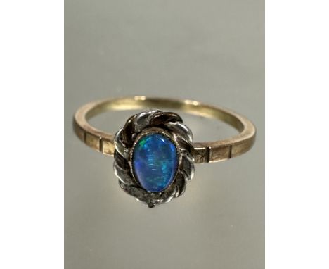 A yellow and white metal artisan made ring, set oval black opal enclosed in rub over setting and rope pattern border, P, (L x