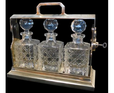 An early 20thC silver plated three division Tantalus, enclosing three moulded glass decanters, with key, 34cm wide. 
