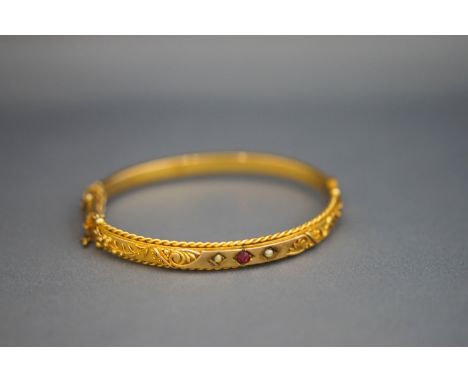 A Victorian unmarked gold hinged bangle, set with a red doublet and two seed pearls, internal diameter 5.7 cm; 8.9 g gross