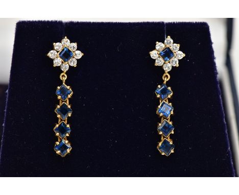 A PAIR OF YELLOW METAL DROP EARRINGS, each earring set with a square cut blue sapphire within a surround of colourless cubic 