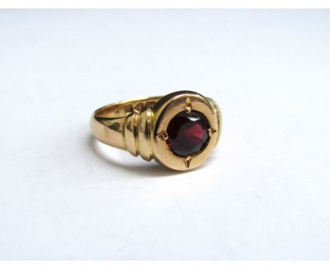 An 18ct gold ring with a round cut garnet in stepped rounded shoulders. Size M, 5.4g 