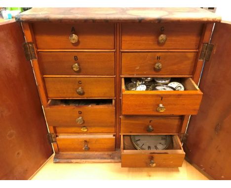 A cabinet of watchmaker's spare parts, watch movements, tools and oddments, circa 1900, the two doors enclosing small drawers