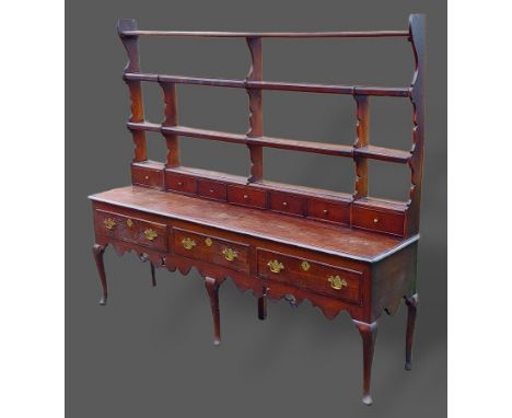 A George III oak dresser, the open shelf back with spice drawers above three drawers with brass handles raised upon turned le