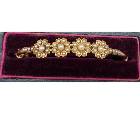 An Edwardian yellow metal bangle set with four pearl clusters and seed pearl shoulders within original box 
