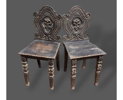 A pair of Victorian carved oak hall chairs, each with a shaped pierced back above a panel seat and raised upon carved front l