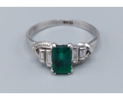 A white metal ring set with a rectangular Emerald flanked by four baguette diamonds, 2gms, ring size M
