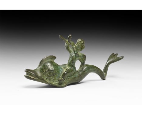1st-2nd century AD. A bronze figure of a dolphin with S-curved body and trident tail, astride its back a nude putto with smal