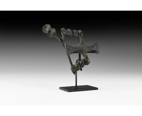 8th-6th century BC. A large bronze fibula with two coils linking by a cruciform plaque, tapering pin, cottonreel finial with 