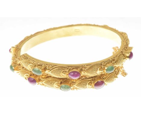 A Balinese gem-set hinged bangleSet with alternating oval ruby and emerald cabochons, to a precious yellow metal bangle with 