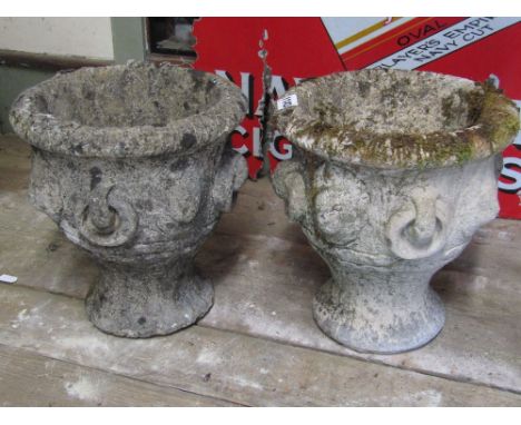 A pair of small weathered composition stone garden urns of circular waisted form with repeating lions marks and ring handles,