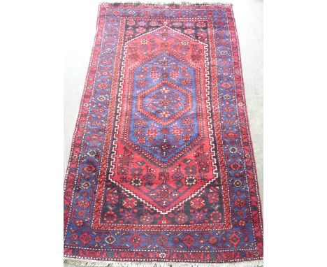 A hand knotted Persian Carpet, the central blue lozenge with stylised patterns within a larger red lozenge and black spandrel