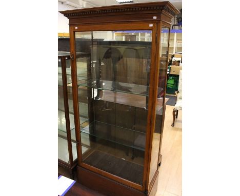 An Edwardian mahogany shop display cabinet, plain dentil moulded projected cornice, fitted with a single door, enclosing two 