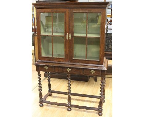 A William and Mary period or later walnut cabinet on stand, fitted with two glazed doors enclosing a fitted shelf, three draw