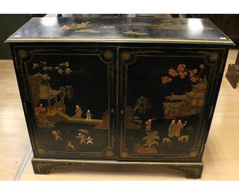 A Japanese style black lacquered side cabinet, fitted with two doors depicting figures in a garden setting, standing on brack