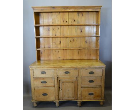 A 19th Century Pine Dresser, the boarded shelf back above a central panel door surrounded by seven drawers with oval brass ha