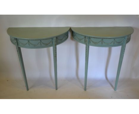 A Pair of Carved and Painted Demi Lune Console Tables, the plain tops above a frieze decorated with bows and swags raised upo