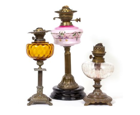 A VICTORIAN OIL LAMP with pink glass reservoir and reeded brass column support, 45cm high together with two further smaller o