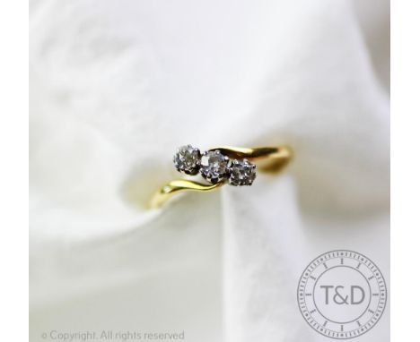 A three stone diamond ring, the three graduated diamonds in diagonal cross-over setting, all claw set in white metal to the t