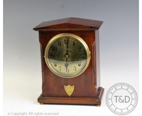 A George V mahogany cased eight day mantel clock, with architectural case enclosing a circular brass face with black Arabic n