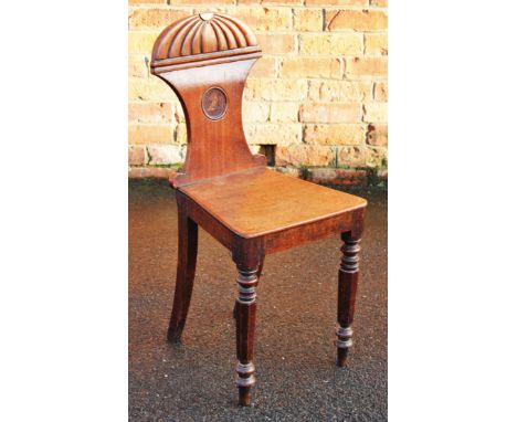 A Regency mahogany hall chair, the shaped back with a painted armorial, above a solid seat, on turned legs, (old worm holes),