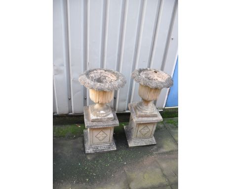 A PAIR OF COMPOSITE GARDEN URNS with acanthus leaf detailing to urn standing on square columns 90cm high