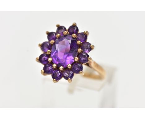 A 9CT GOLD AMETHYST CLUSTER RING, of an oval form, set with a central oval cut amethyst within a surround of circular cut ame