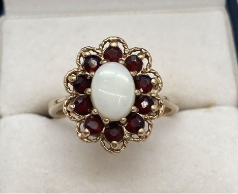 A 9ct gold dress ring set with central oval opal and surrounded by a ring of garnets. Framed with a gold rim. Fully hallmarke