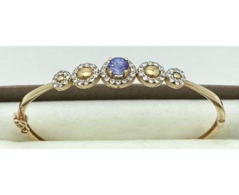 A 14ct gold hinged bangle with stone set flower design to top. Central oval iolite stone surrounded by small round cut clear 