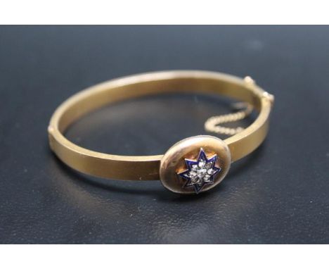 A 15CT DIAMOND AND ENAMEL BANGLE, having a central diamond surrounded by 8 diamonds and these in turn are surrounded by a blu