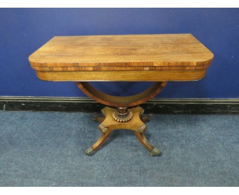A REGENCY ROSEWOOD FOLD-OVER CARD TABLE, opening to a green baize surface, raised on a demi-lune support and four outsplayed 