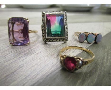 A group of four rings to include a yellow metal and amethyst ring, a 9ct gold and opal three stone ring, a yellow metal ruby 