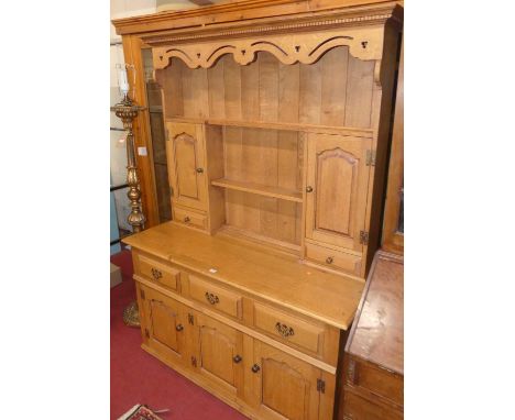 A contemporary joined light oak dresser, having twin shelves, recessed panelled cupboard doors and short drawers, over base f