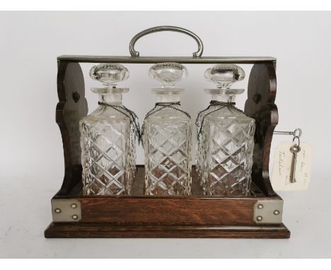 An Edwardian oak and cut glass tantalus, with three diamond pattern glass decanters with multiple ceramic labels