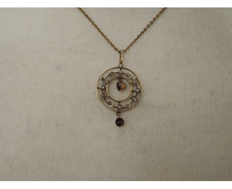 An Edwardian yellow metal pendant and chain stamped 9ct of circular form having garnet and seed pearl decoration