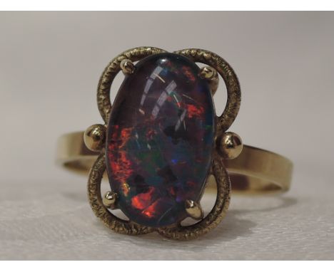 A lady's dress ring having an oval black opal doublet stone in a claw set open basket mount on a yellow metal loop stamped 9c