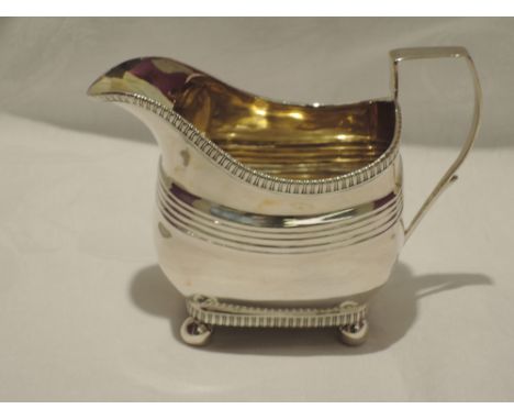 A Georgian silver sugar cream jug of shaped oblong form having gadrooned rim, reeded decoration, architectural and quill hand