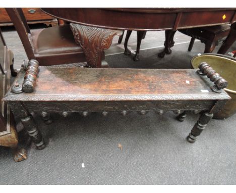 A late Victorian dark oak hall seat having carved decoration and bobbin arms and turned legs