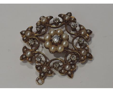 An Edwardian yellow metal pendant/brooch stamped 15ct of open circular form having diamond and seed pearl decoration