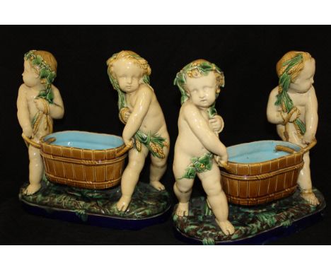 A pair of 19th Century Minton majolica table pieces as putti carrying coopered wine coolers raised on a leafy elongated oval 