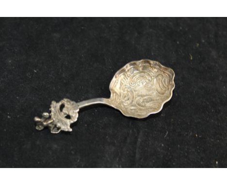 An 18th Century Continental white metal caddy spoon, the handle set with dancing cherubic figure set upon a crown to a shell-