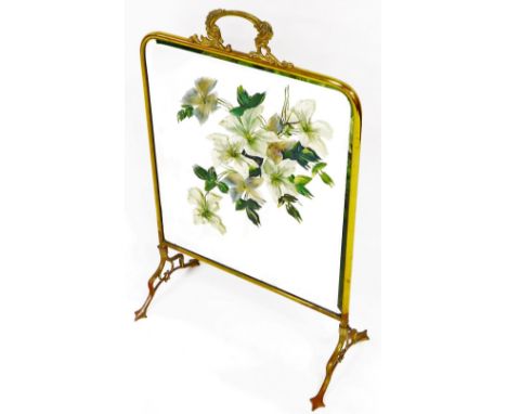 An early 20thC brass framed fire screen, with painted glazed centre set with flowers on shaped legs with inverted heart shape