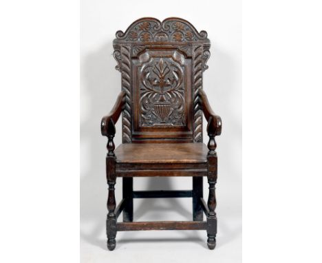 An early 18c oak open armchair with shaped downswept arms with baluster turned supports, having solid seat and a carved back 