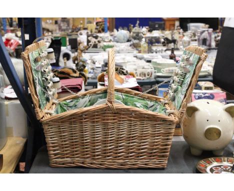 A WICKER PICNIC BASKET WITH LEAF PATTERN INTERIOR TO INCLUDE KNIVES, FORKS, SPOONS, PLATES, SALT AND PEPPER POTS, PLASTIC WIN