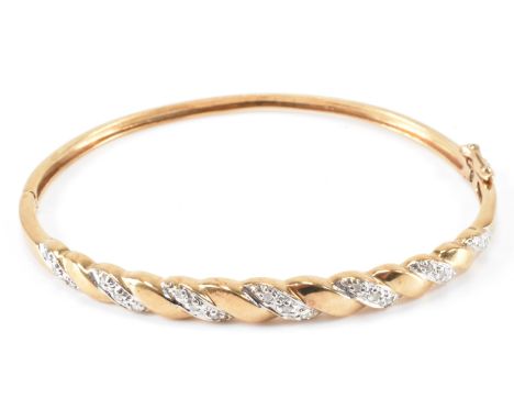 A gold and diamond two tone bangle bracelet. The bracelet having a two tone twist design head set with diamond accent stones.
