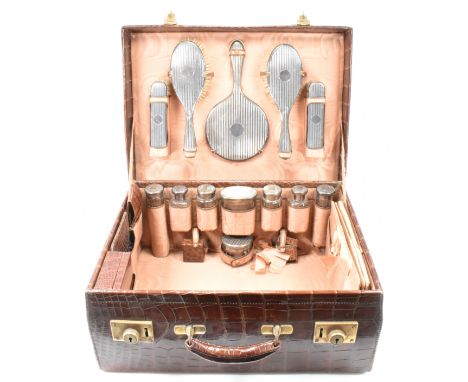 An early 20th century silver dressing table set in a crocodile skin vanity case. The set to include two silver hair brushes, 