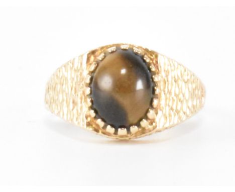 A 1970s hallmarked 9ct gold tigers eye ring. The ring having a cabochon tigers eye on a textured gold head and shoulders. Hal