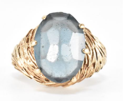 A vintage gold blue stone set ring. The ring having a faceted blue stone on gold domed swirl head and shoulders. Marked 9ct t