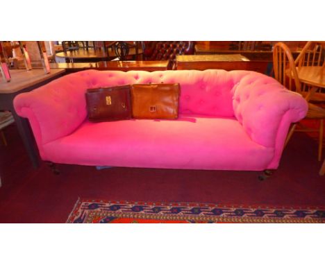 A Victorian Chesterfield sofa upholstered in buttoned pink fabric and raised on turned supports and castors 