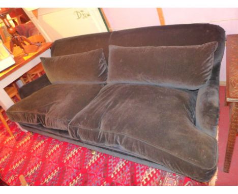 A contemporary Howard style three seater sofa upholstered in black velour and raised on turned supports and brass castors  